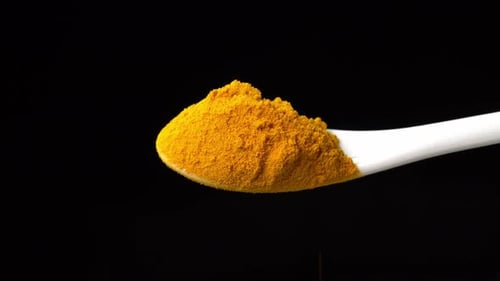 Turmeric Powder spice on a spoon is poured out isolated on a black background. Dry seasoning