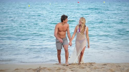 Young Couple Joyfully Walking Hand in Hand Along the Beautiful Sandy Beach Under the Bright Sun