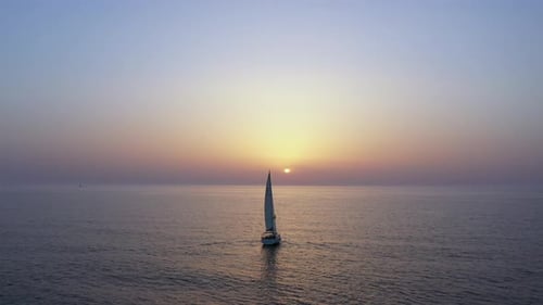 Sail boat sailing slowly towards a setting Sun in the Mediterranean Sea.