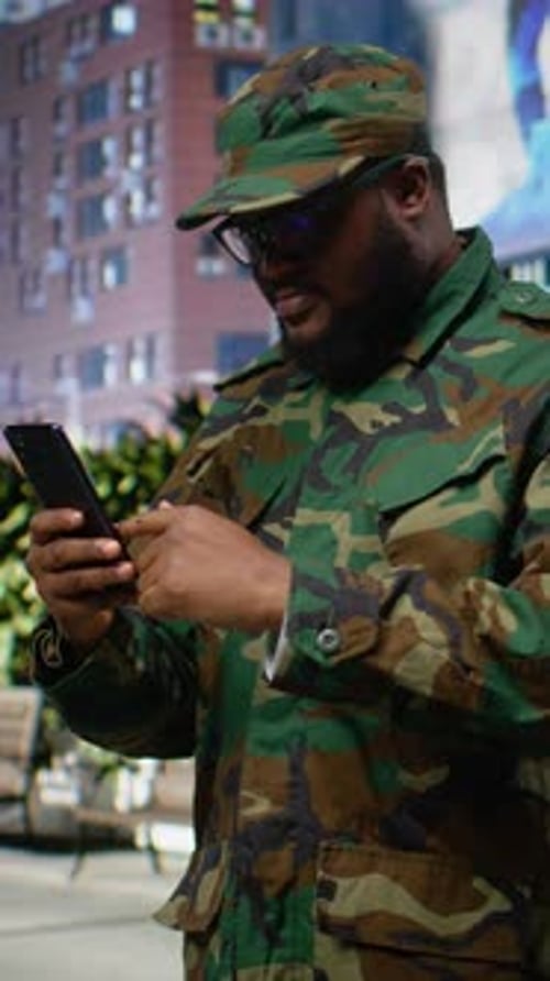 Man in Camouflage Jacket Using Phone in City
