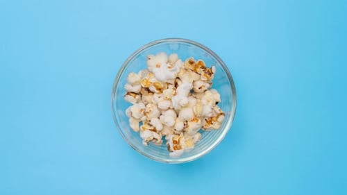 Popcorn Spreading around Bowl on Blue Background