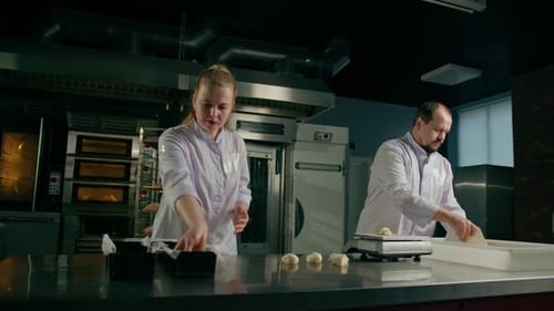 dos panaderos dan forma a la masa cruda antes de hornearla, la cortan y la despliegan sobre la mesa de cocina profesional