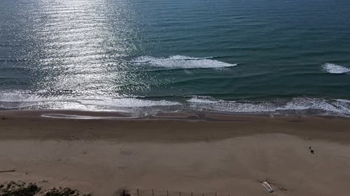 Serene beach view at midday with gentle waves lapping at the shore and sunlight glistening on the wa