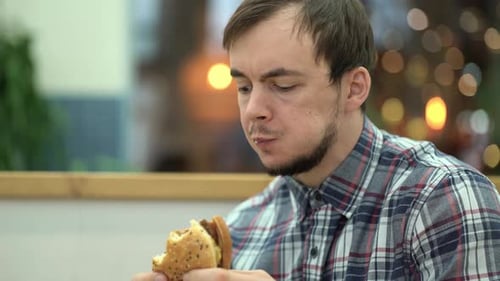Unshaven Man Eats Meat Big Burger on Fast Food Restaurant