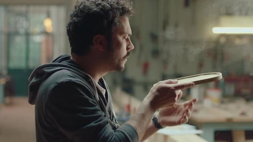 Man Inspecting Wooden Carving in Workshop