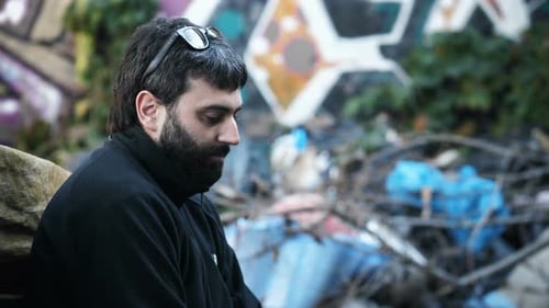 Depression, Einsamkeit - verzweifelter Mann, der neben einem Müllhaufen sitzt, schaut nach unten