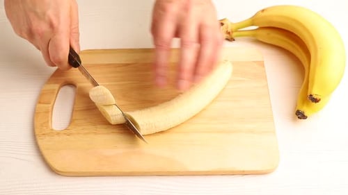 Hands Slicing Banana on Cutting Board