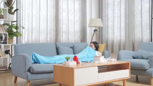 Femme asiatique malade avec une couverture souffrant de toux alors qu'elle est allongée sur le canapé dans le salon à la maison
