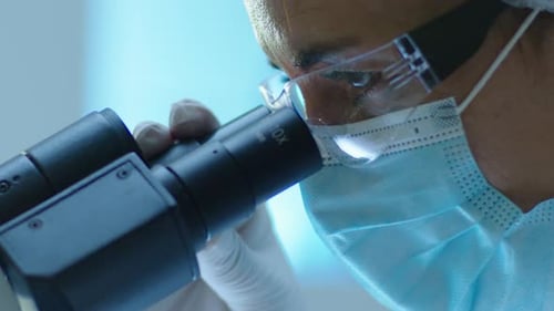 Close-Up of Female Lab Scientist In Mask and Gloves Using Microscope