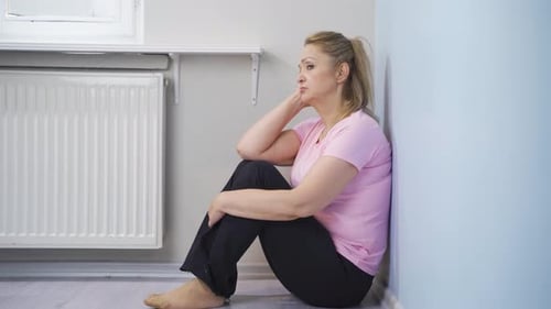 Blonde Woman Sitting Against Wall in Home