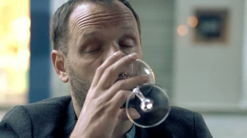 Inebriated young man sits alone drinking red wine in a city cafe on a difficult day