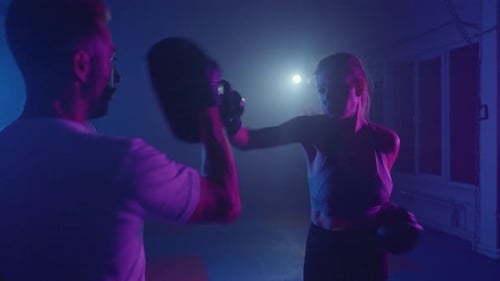 Intense Boxing Training Session at a Neonlit Gym with a Dedicated Female Athlete and Her Coach