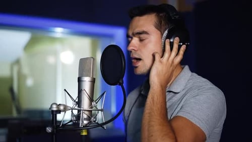 Caucasian singer wearing headphones holding them with his hands sings.