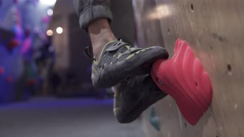 Legs of a man in sports shoes steps on artificial stones on a climbing wall, close-up.
