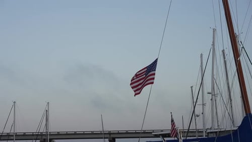 American Flag Waving near Sailboats and Bridge