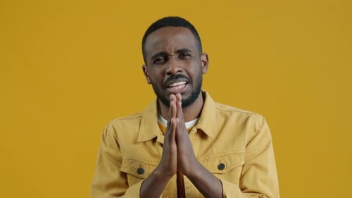 Man Pleading with Hands Together Against Yellow Background