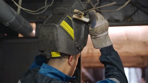 Close Up Shot of Professional Welder in Safety Suit and Protective Mask Starts Welding Flat Metal