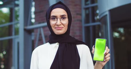 Close Up of Confident Muslim Woman in Black Hijab and Glasses Holding Smartphone with Greenscreen