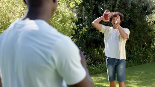 Playing catch with football, two multiracial male friends enjoying outdoor hangout in park