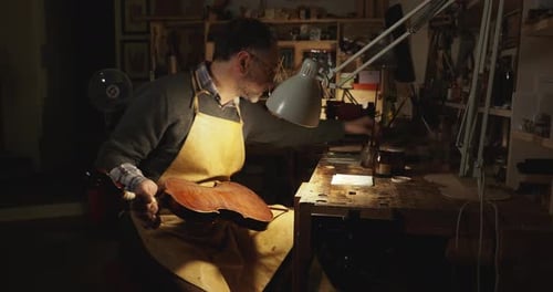 Master Luthier violinmaker apply coating with tampon on handcrafted stringed instrument in workshop