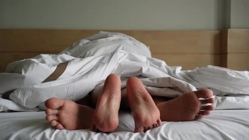 Feet of Couple Under White Bedroom Sheets