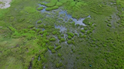 Aerial footage birds eye view flying over the wet marshy land of an island that is just off the coas