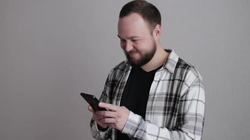 Man with Beard Smiling Using Smartphone Indoors