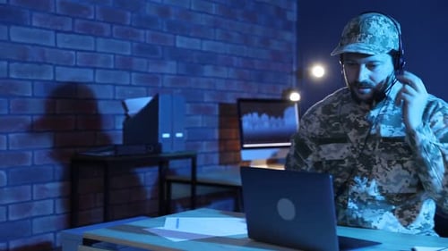 Military service. Soldier in headset working at wooden desk in office at night, camera moving right