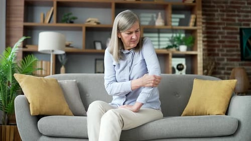 Senior Woman Rubbing Elbow in Pain at Home