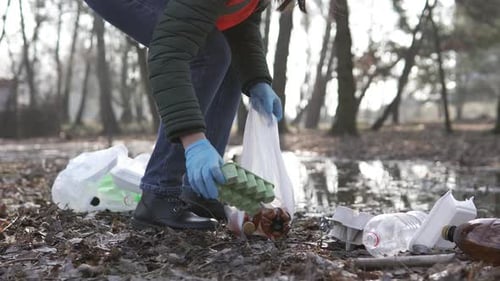 A volunteer collects garbage in the park and takes it to the trash cans.