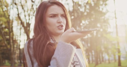 Close Up of Young Charming Caucasian Woman Strolling in Park and Recording Voice Message By
