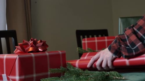 woman wrapping Christmas gifts on a table, with red boxes and a green tablecloth