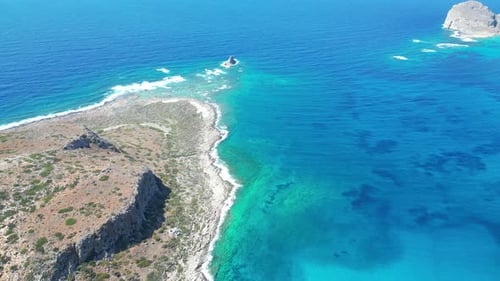 A high-altitude drone captures a stunning view of crystal-clear blue waters and the seabed between t