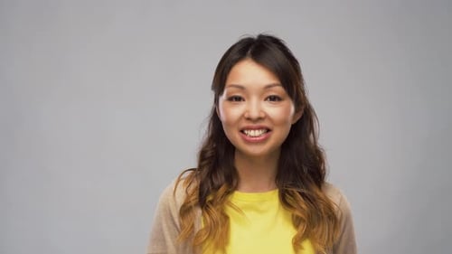 Smiling asian woman talks and answers questions in studio over grey background