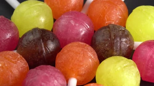 Colorful lollipops or candy bonbons on a stick rotating on black plate in macro top view. Holiday