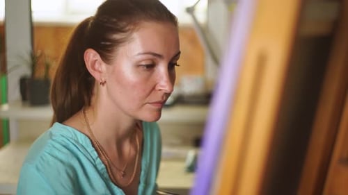 A adult female brunette artist paints a painting on canvas in her creative studio.