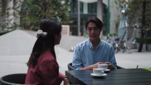 Young Asian Couple Talking and Drinking Coffee at Outdoor Cafe