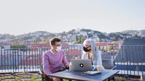Businesspeople in city wearing face masks working on laptops outdoors