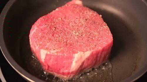 Juicy beef steak sizzling on a hot grill sprinkled with salt and pepper slow motion