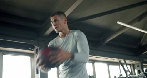 Focused Young Man Training With Medicine Ball in Modern Gym