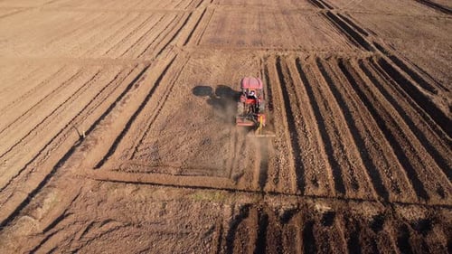 Aerial view of fields and agricultural parcels. Farmer in tractor preparing land with seedbed