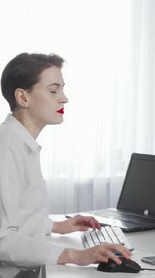 Focused Female Freelancer Multitasking with Smartphone and Laptop in a Bright Office