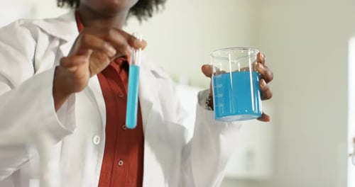 En soulevant le tube à essai, le scientifique stabilise le bécher et le tube tout en comparant le liquide bleu sur un banc