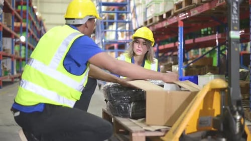 Warehouse workers inspect goods together on pallet trucks in a large warehouse
