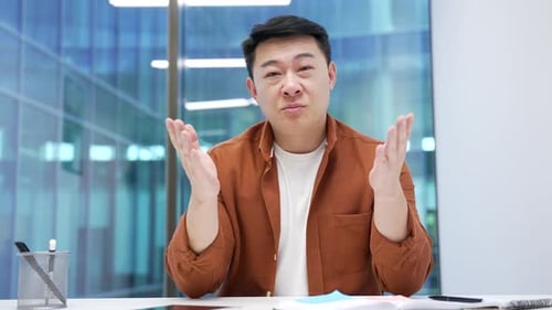 Webcam view. Confident asian businessman talking on a video call looking at camera sitting at workpl