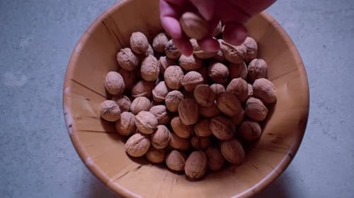 Hand sifting through walnuts in wooden bowl