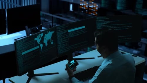 Happy Man Looking At Code On Mobile Phone While Write Code With Multiple Computer Screens In office