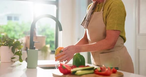 Senior Woman Washing Colorful Vegetables in Sunny Kitchen