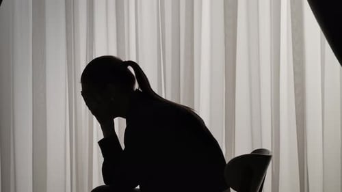 Silhouette of a Distressed Woman in Front of Backlit Curtains