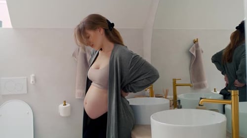 Pregnant Woman Massaging Lower Back in Bathroom